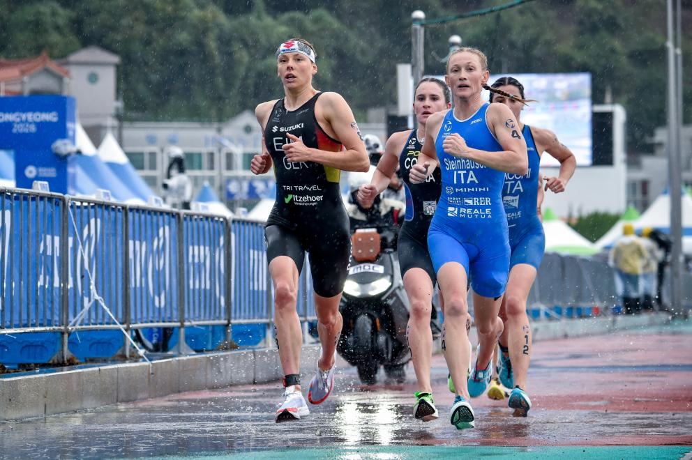 Mehrere weibliche Triathletinnen laufen auf regennasser asphaltierter Straße