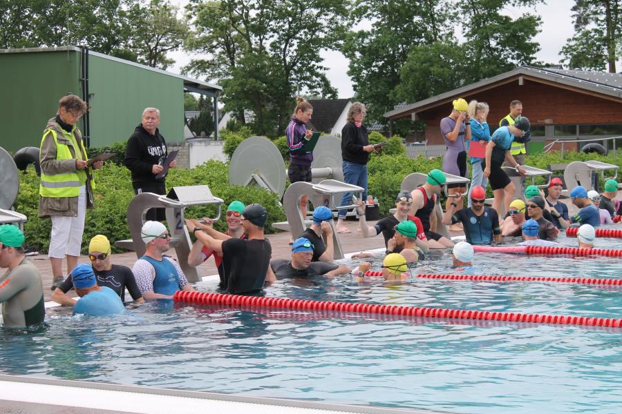 Athleten im Schwimmbecken und Zeitnehmer sowie Helfer und Kampfrichter am Beckenrand beim Büchen Triathlon