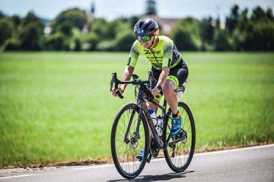 Janine Langer sitzt im schwarze gelben Trisuit auf dem Rad im Hintergrund grüne Wiese