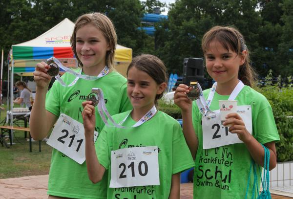 Drei Kinder im grünen Shirt zeigen ihre Medaillen und freuen sich