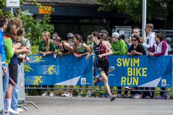 Athletin läuft um Kurve und blickt nach hinten, im Hintergrund viele Leute, die anfeuern