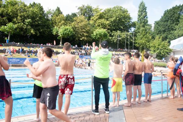 Kinder und Trainer stehen am Beckenrand und feuern an