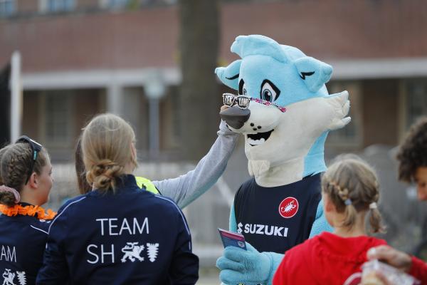 Kinder setzen Maskottchen Trinity eine Sonnenbrille auf