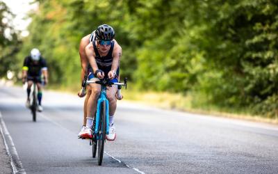 Ein Tandem fährt auf einer Straße, dahinter fährt ein einzelner Radfahrer