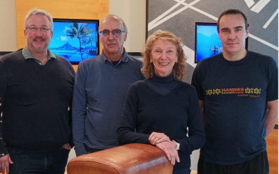 Drei Männer und eine Frau posieren an einem kleinen Turngerät, dem Turnpferd, für ein Foto