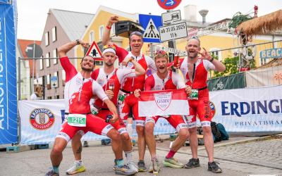Fünf Triathleten jubeln gemeinsam im Zielbereich einer Veranstaltung posierend in die Kamera