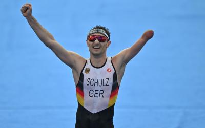 Ein Para Triathlet, dem der linke Unterarm fehlt, jubelt im Ziel eines Triathlons mit nach oben gestreckten Armen
