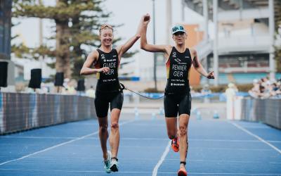 Zwei Triathletinnen überqueren gemeinsam, sich an der Hand haltend die Ziellinie