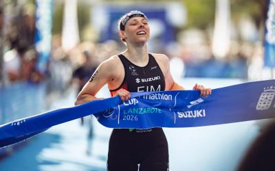 Eine Triathletin läuft glücklich mit dem Zielband in der Hand zum Sieg