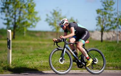 Junge Triathletin auf dem Rennrad mit grüner Wiese und Bäumen