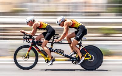 Ein Rennrad-Tandem mit einem Guide und einer sehbeeinträchtigen Sportlerin im deutschen Trikot in rasanter Fahrt