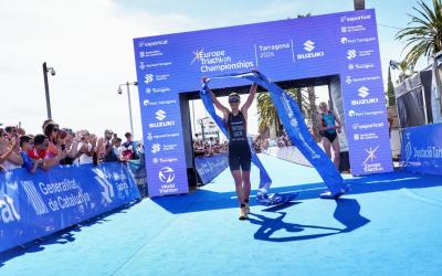 Triathletin läuft mit hochgestreckten Armen und Zielbanner in den Händen unter Zielbogen