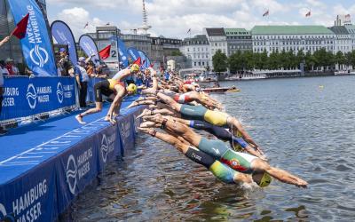 Zahlreiche Männer springen bei einem Triathlon nach dem Startschuss ins Wasser