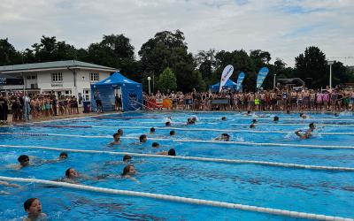 Kinder Schwimmen im Freibad und werden von den anderen Kindern angefeuert
