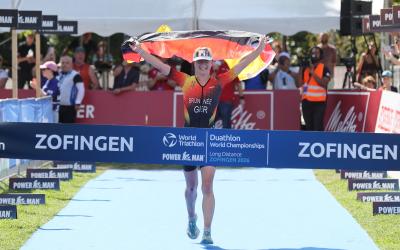 Eine Sportlerin in deutschem Dress läuft freudestrahlend mit der Deutschlandfahne in der Hand dem Sieg bei einem WM-Rennen entgegen