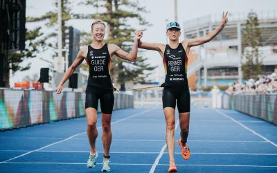 Eine sehbeeinträchtigte Para Triathletin läuft gemeinsam mit ihrer Guide jubelnd über die Ziellinie eine Triathlons