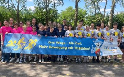 Mehrere Menschen stehen hinter einem Banner mit dem Slogan: "Drei Wege - ein Ziel: Mehr Bewegung mit Triathlon!"