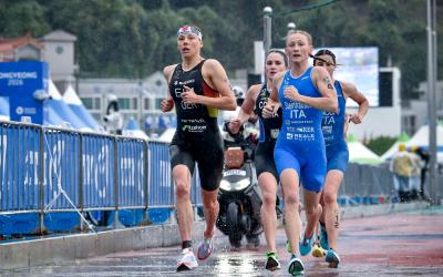 Mehrere weibliche Triathletinnen laufen auf regennasser asphaltierter Straße